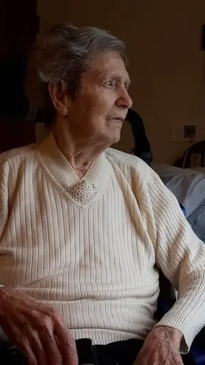 Elderly woman (Eileen High) wearing a light white sweater, gazing to the right of the camera's perspective.