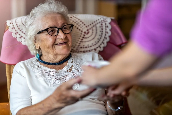 Smiling elderly woman reaching out to nurse while sitting down