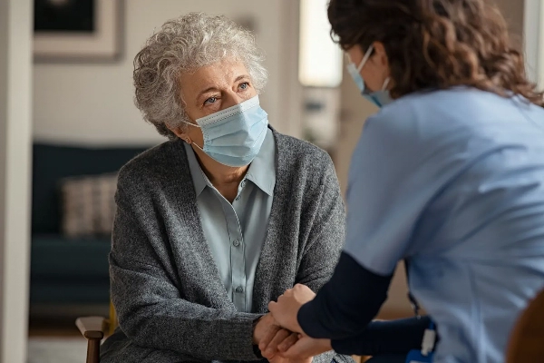 Nurse holding hands with elderly woman; both wearing face masks